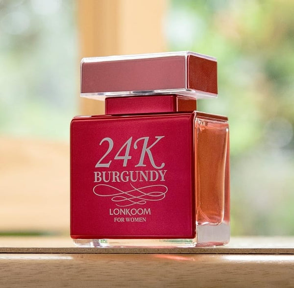 Red perfume bottle labeled '24K Burgundy' by Lonkoom on a wooden surface with a blurred natural background.